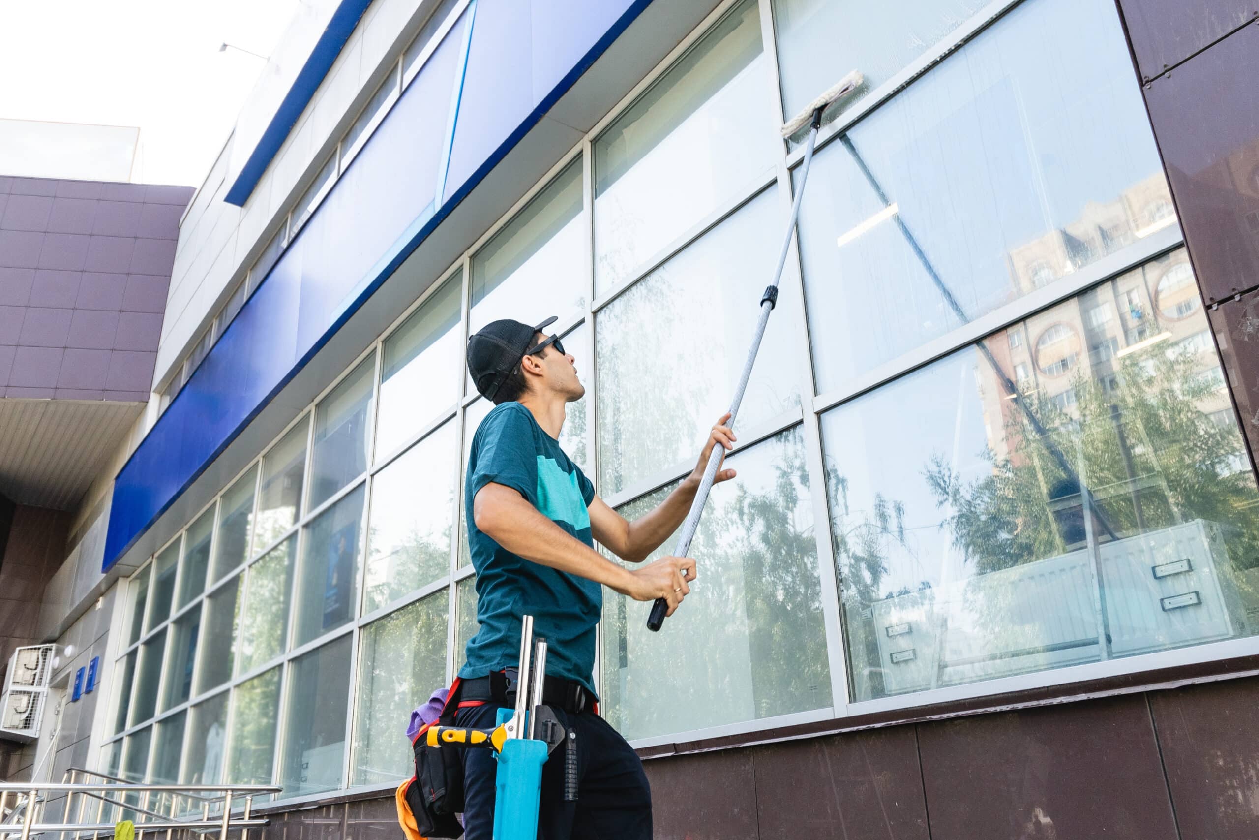 An employee of a professional cleaning service in overalls washes the facade and windows with special devices