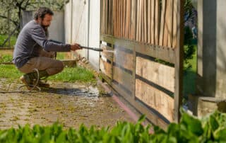 Mid adult man cleaning a wooden gate with a power washer